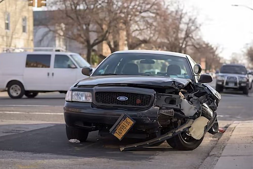 A damaged black Ford car with a dislodged license plate on a road, emphasizing the aftermath of a hit-and-run accident and road safety.