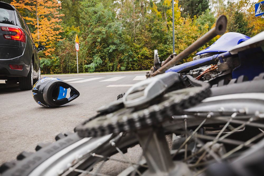A motorcycle accident scene with a fallen bike, blue helmet, and a car nearby.